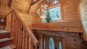 A wooden cabin interior with a staircase, a chandelier, a Christmas tree, and a window with a view of trees. - My Happy Place - Lakefront cabin (New Tazewell)