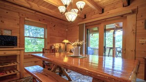 A wooden cabin interior with a large dining table, benches, and a chandelier. - My Happy Place - Lakefront cabin (New Tazewell)