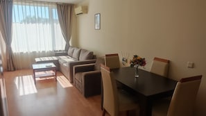 A living room with a sofa, a coffee table, a dining table with chairs, and a window with curtains. - Apartment - Sleeps 6, Pet Friendly & 6 Pools (Nessebar)