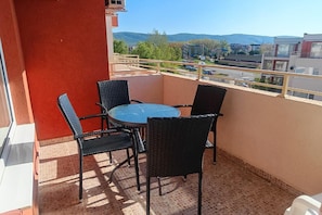 A balcony with a round table and four chairs, overlooking a street and distant hills.