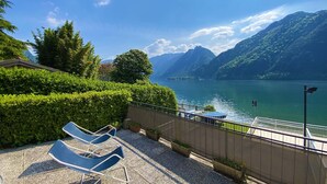 A terrace with lounge chairs overlooking a lake, surrounded by greenery and mountains. - Directly on the lake with terrace (Tre Capitelli)