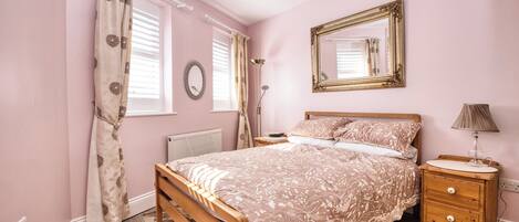 A bedroom with a wooden bed, a nightstand, a lamp, and a mirror on the wall.