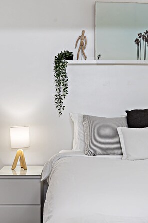 Ein ordentlich eingerichtetes Schlafzimmer mit einem Bett, einem Nachttisch mit Lampe, einer hängenden Pflanze und einer Holzmannequin.