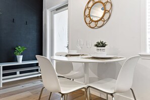 A modern dining area with a round table, white chairs, and a decorative mirror on the wall. - Charming Apartment in Las Olas Blvd Isle (Fort Lauderdale)