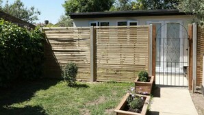 A wooden fence with a gate, a small garden area with plants, and a building with a window and a door.