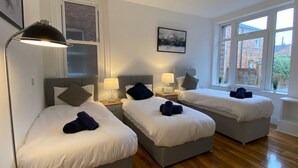 Camera d'albergo con due letti, ognuno con cuscino e coperta. Una finestra offre vista sugli edifici.