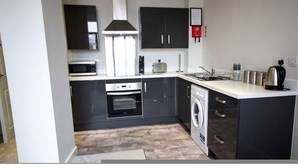 A compact kitchen with a microwave, oven, toaster, and a washing machine. - Stayzo Self Catering Accommodation 3 -bradford UK (Bradford)