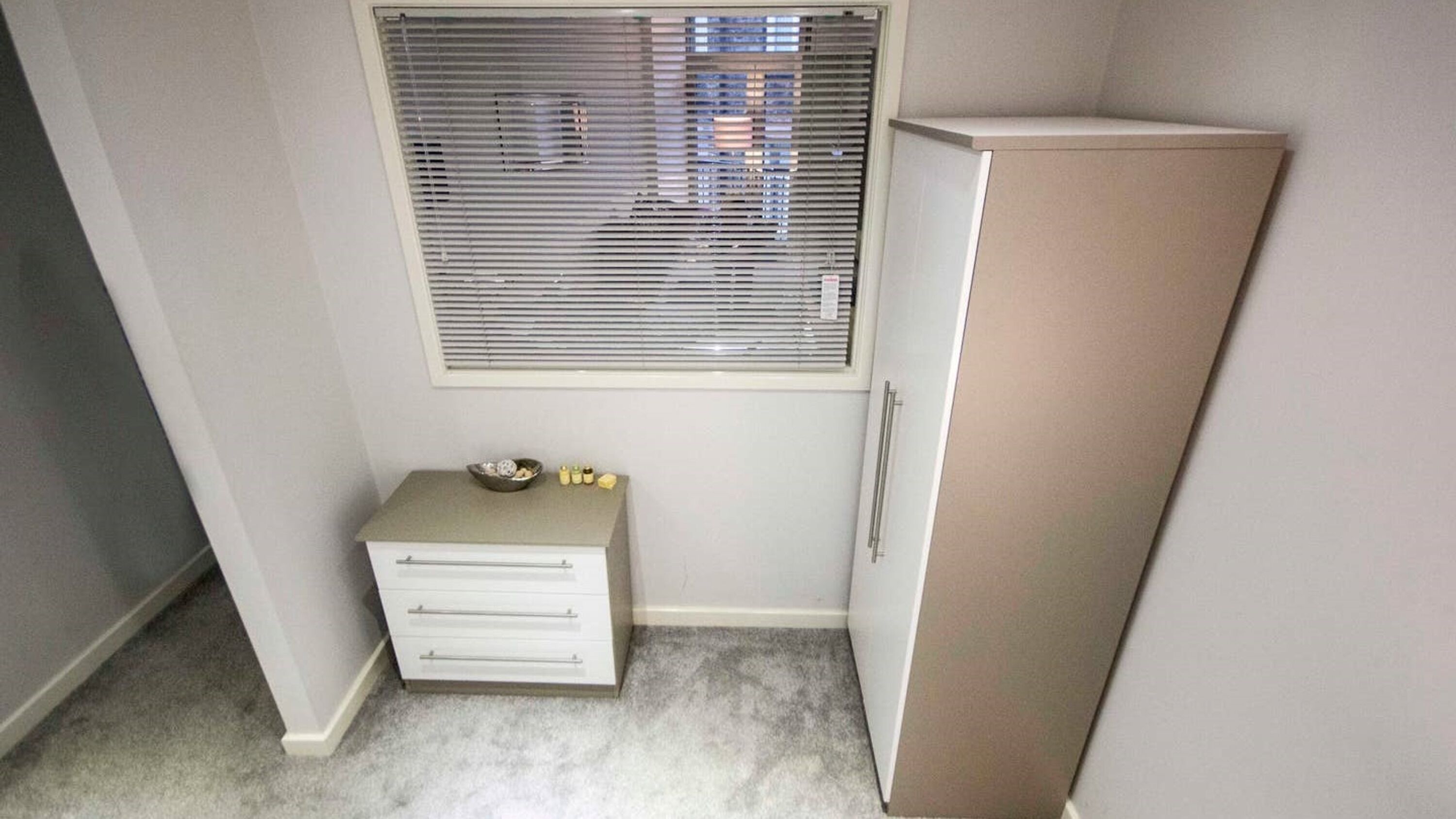 A small room with a white dresser, a cabinet, and a window with blinds.