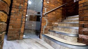 Una escalera con barandilla de metal, paredes de ladrillo y suelo de baldosas.
