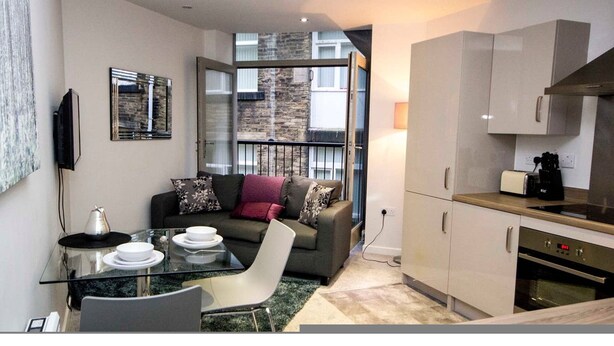 Un espacio habitable compacto con comedor, sofá, cocina con armarios blancos y balcón con pared de piedra.