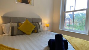 A neatly made bed with a grey headboard, a yellow pillow, and a bedside lamp. - De Parys Premier Lodge 3 in Bedford (Bedford)