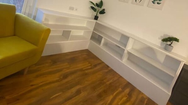 A room with a yellow armchair, wooden flooring, white built-in shelving, and small potted plants. - De Parys Premier Lodge 3 in Bedford (Bedford)