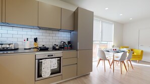 A modern kitchen with a built-in oven, a stovetop, and a dining area with a table and chairs. - Luxury Apartment - Town Centre North Stevenage (Stevenage)