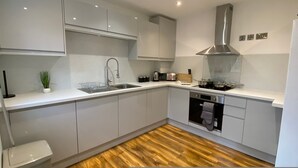A modern kitchen with white cabinetry, a stainless steel range hood, and a wooden floor.