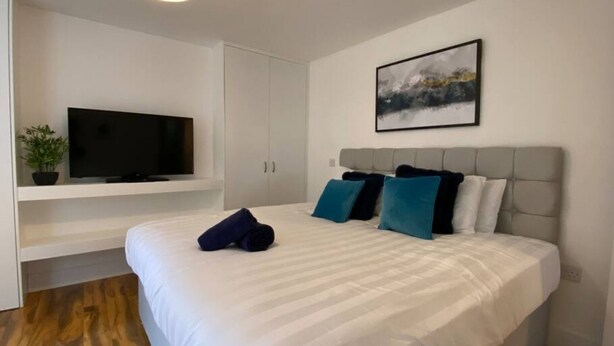 A modern hotel room with a large bed, a flat-screen TV, a painting, and a potted plant.
