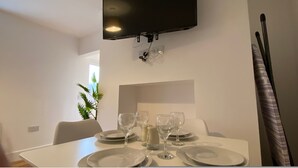 A dining area with a table set for four, a flat-screen TV mounted on the wall, and a potted plant in the corner.