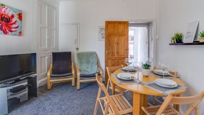 Un coin repas avec une table en bois dressée pour quatre personnes, un téléviseur et une porte donnant sur l’extérieur.