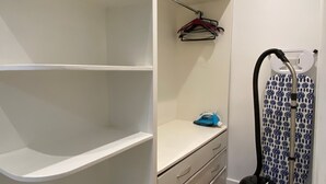 Ein Kleiderschrank mit Regalen, einer Kleiderstange und einem kleinen Bügelbrett mit Bügeleisen.