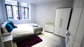 A bedroom with a bed, a dresser, a wardrobe, and a window with blinds. - Stayzo - Executive City Centre Apartment 2 (Bradford)
