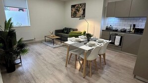 A modern living room with a dining area, a green sofa, a coffee table, and a view of the kitchen.