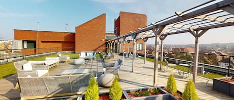 Terraza en la azotea con mobiliario exterior, una pérgola y vistas a la ciudad.