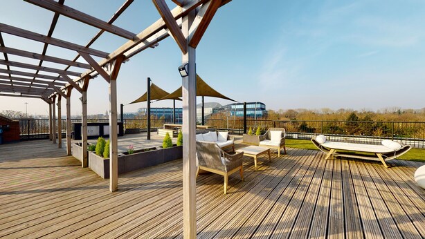 A wooden deck with outdoor furniture, a pergola, and a view of a modern building in the background.