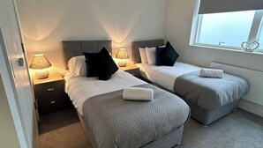 A hotel room with two single beds, each with a headboard, bedside tables with lamps, and a window with a heart-shaped decoration.