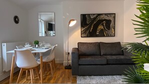 Un salon moderne avec un canapé gris foncé, une table à manger avec des chaises blanches, un lampadaire et un grand tableau abstrait accroché au mur.