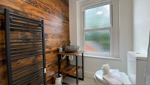 Une salle de bain avec un mur en bois, une fenêtre donnant sur un paysage agréable, un lavabo avec un receveur en pierre et des toilettes.