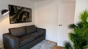 Une pièce avec un canapé gris foncé, une œuvre d’art en marbre, une porte blanche et une plante verte.