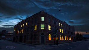Een historisch bakstenen gebouw met meerdere verlichte ramen, een opvallende ingang en een straatnaambord dat nabijgelegen locaties aangeeft.