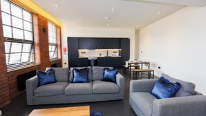 Een moderne woonkamer met een grijze zithoek, een houten salontafel en een eethoek met een tafel en stoelen.