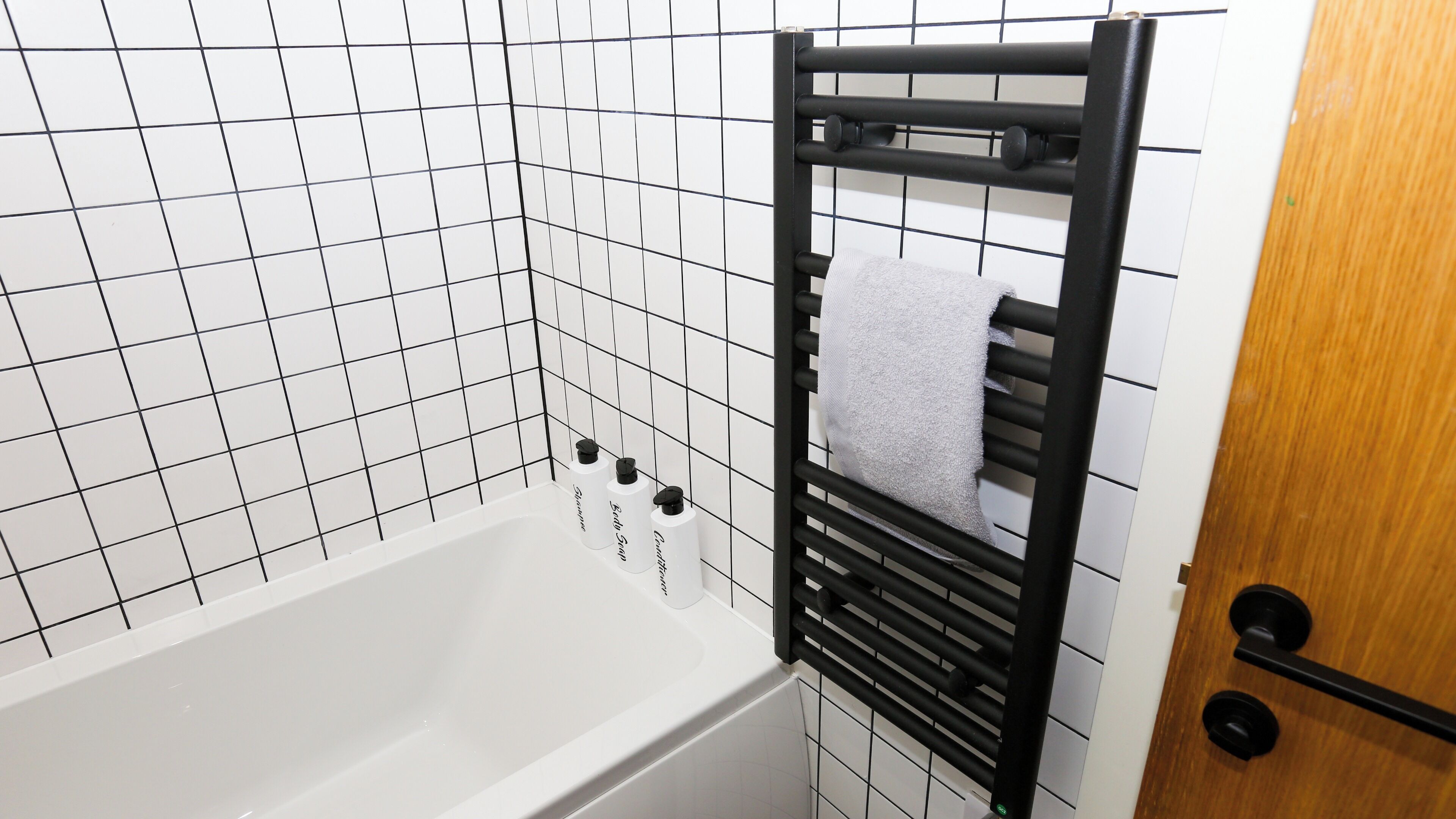A bathroom with a white bathtub, black towel rack, and a door with a round handle.