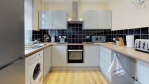 A compact kitchen with a washing machine, oven, microwave, and toaster. - Stayzo Westminster Stylish House Accommodation (Bradford)