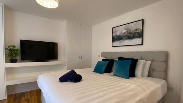 A modern hotel room with a large bed, a flat-screen TV mounted on a white wall, and a painting above the bed. - Stayzo Westminster Stylish House Accommodation (Bradford)