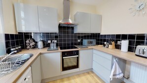 A modern kitchen with white cabinets, a stainless steel range hood, a microwave, a toaster, and a dish rack. - Stayzo Westminster Stylish House Accommodation (Bradford)