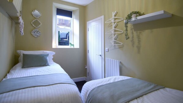 A bedroom with two beds, a window, a door, and a radiator.