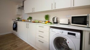 Cocina compacta con armarios blancos, horno integrado, microondas y lavadora de carga frontal.