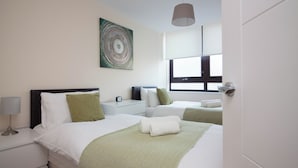 Habitación de hotel con dos camas, una mesita de noche con lámpara, un cuadro en la pared y una ventana con vistas.