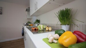 Una cocina moderna con gabinetes blancos, un lavamanos de acero inoxidable y una variedad de verduras frescas sobre la encimera.