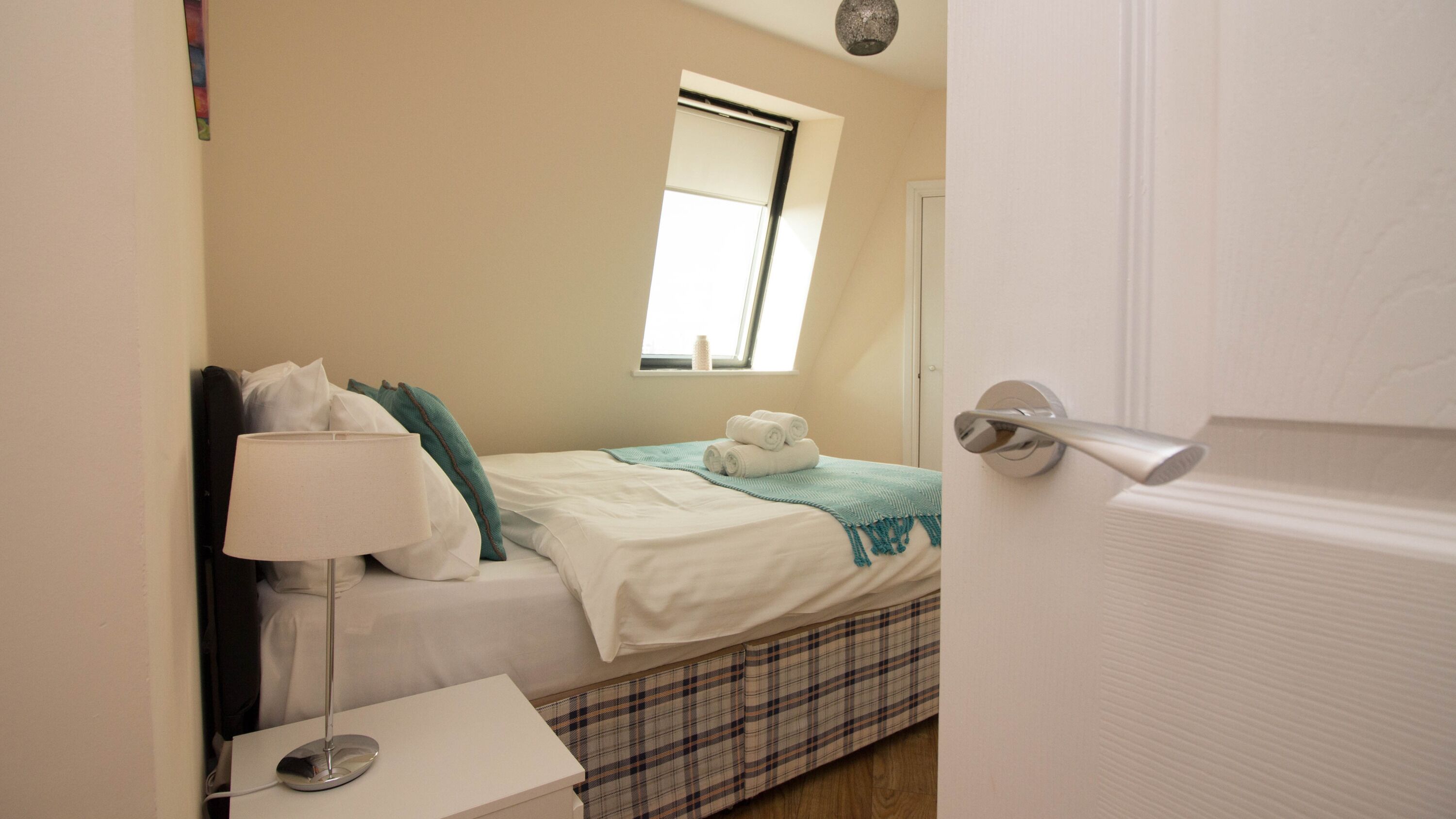 Un dormitorio con cama, mesita de noche con lámpara, ventana y puerta.