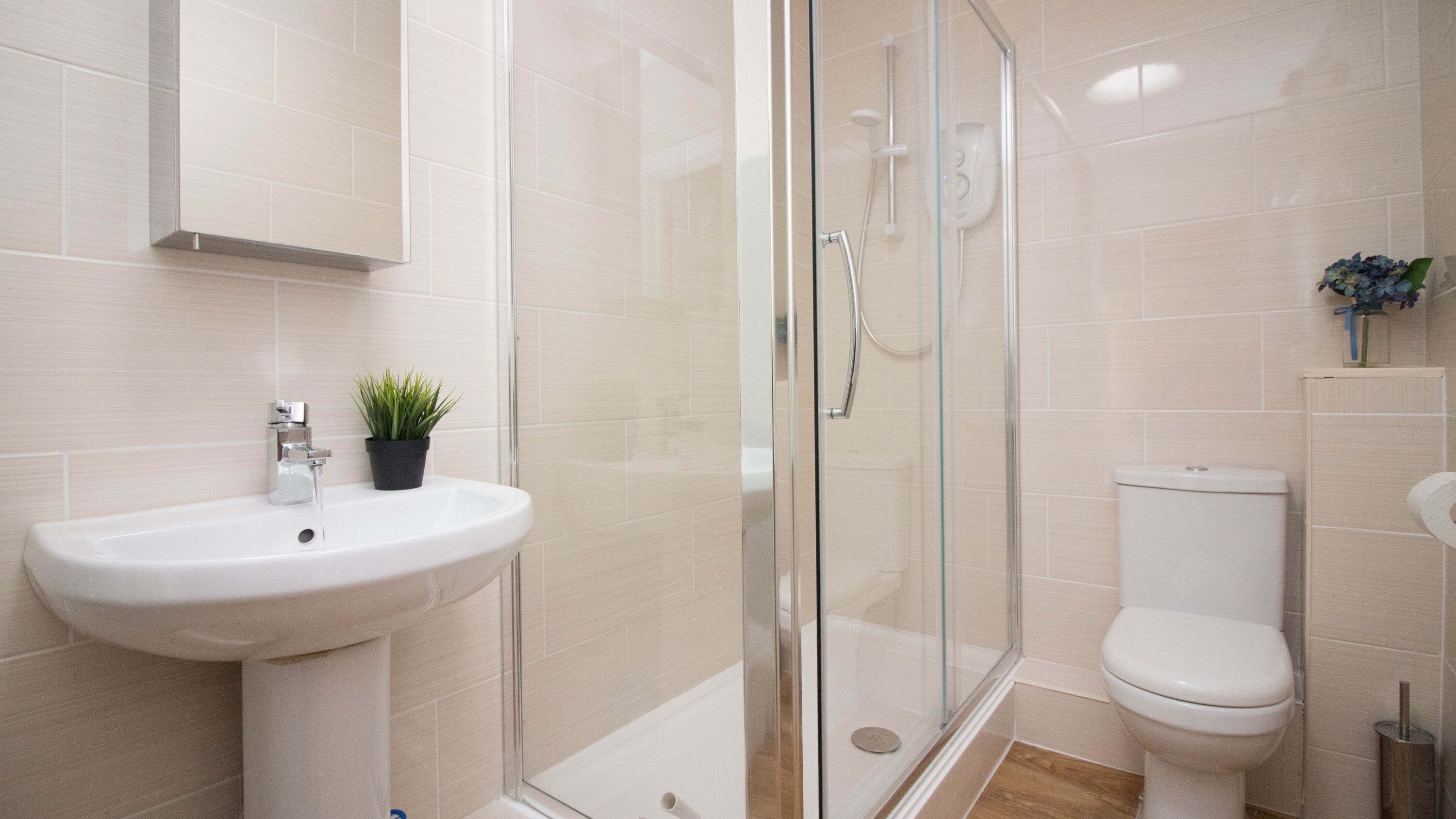Un baño moderno con ducha envuelta en cristal, lavamanos blanco y retrete.