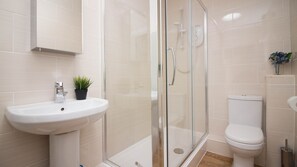 Un baño moderno con ducha envuelta en cristal, lavamanos blanco y retrete.