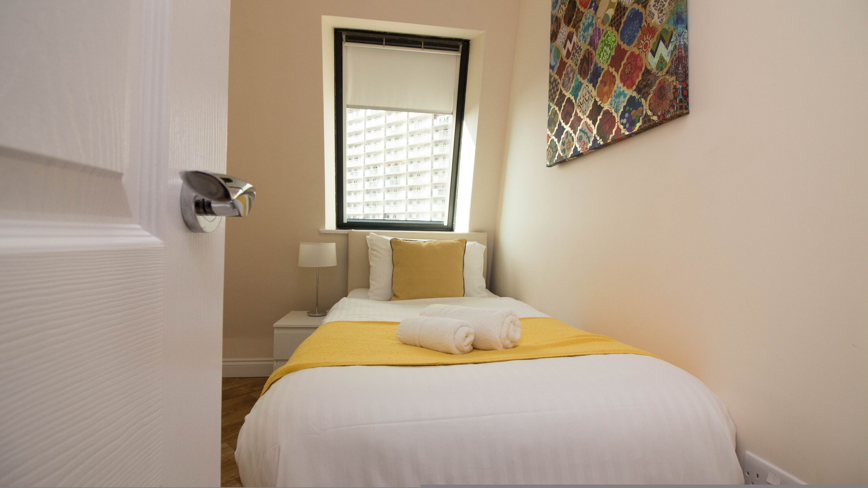 Una habitación de hotel con una cama, una ventana, una mesita de noche y una obra de arte colgada en la pared.