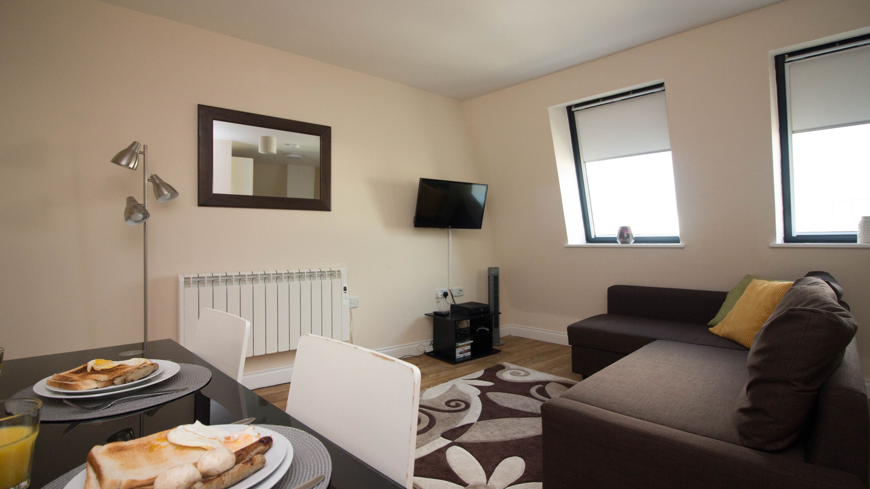A modern living room with a sofa, a dining table with breakfast, a TV, and a window.