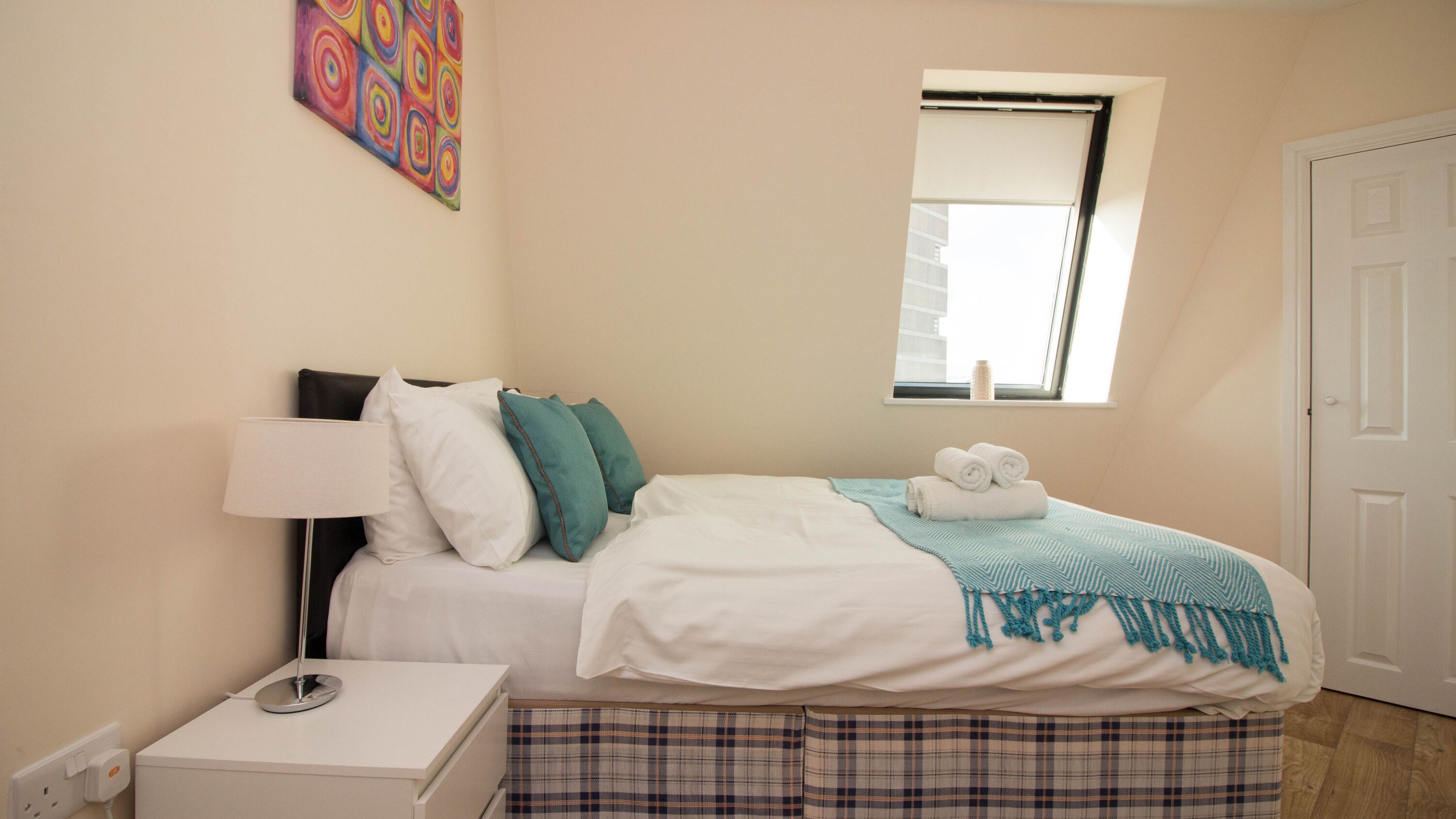 Une chambre à coucher avec un lit, une table de chevet, une lampe, une fenêtre et une porte.
