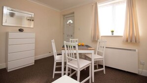 A room with a dining table, four white chairs, a white dresser, a window with curtains, and a radiator.