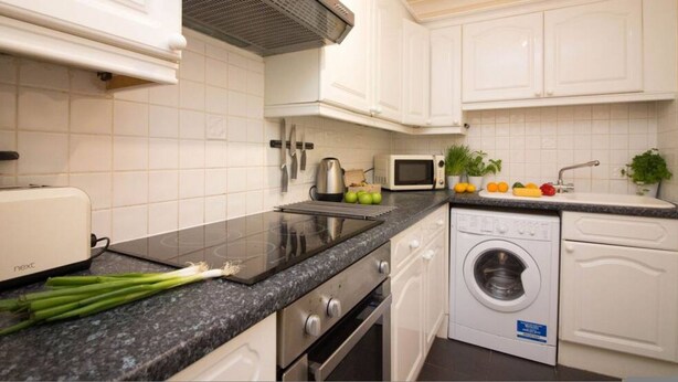 A modern kitchen with white cabinets, a built-in microwave, a toaster, and a washing machine.