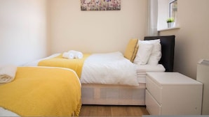 A bedroom with two beds, a bedside table, a window with a view, and a small plant on the windowsill.