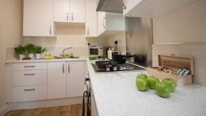 A modern kitchen with white cabinets, a stainless steel range hood, a microwave, and a wooden box with snacks. - Stayzo Castle Point 18 Apartments - Premier Lodge (Southampton)